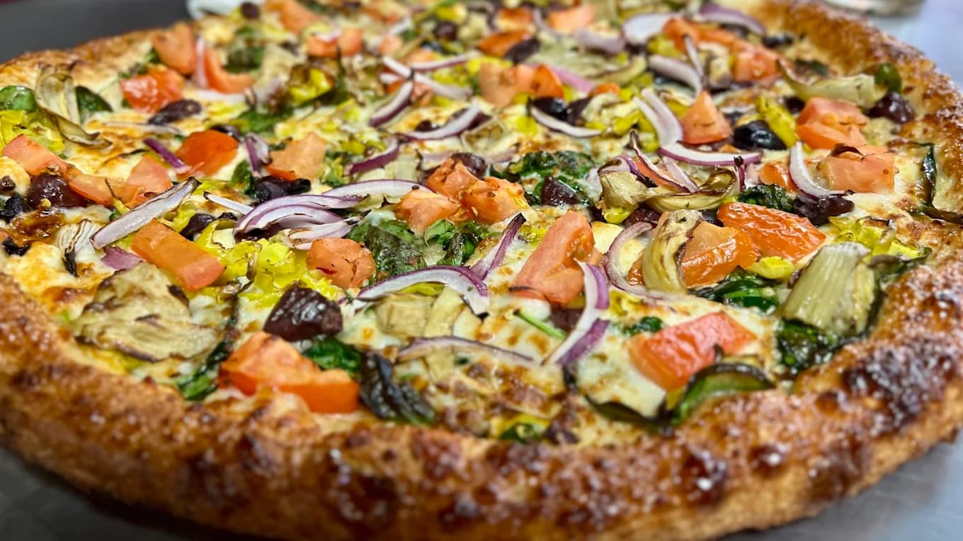 Close-up of a 19th Street Pizzeria pizza topped with tomato, red onion, spinach, artichoke and olives