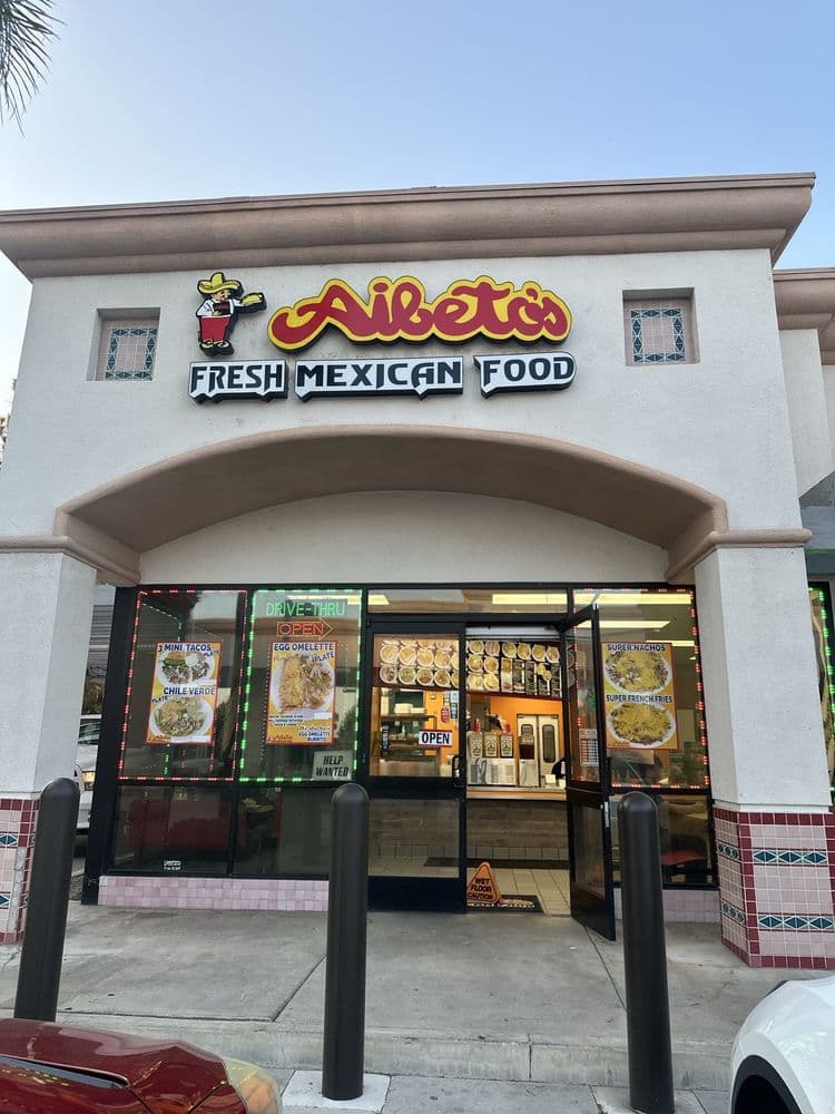 The Aibeto's Fresh Mexican Food storefront, its lit sign above an arched entry, with menu posters and a drive-thru sign in the windows