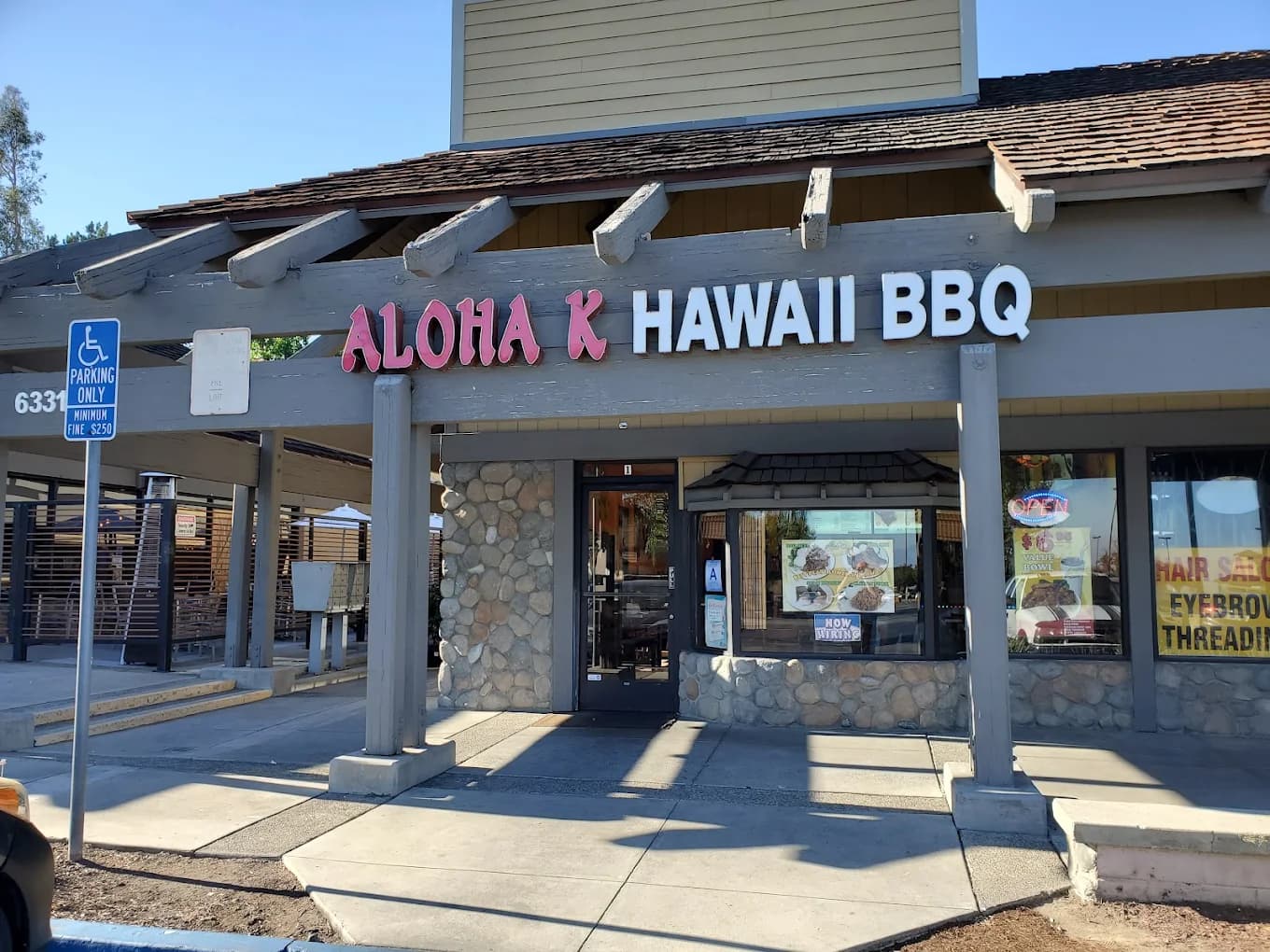 Storefront of Aloha K Hawaii BBQ with pink and white lettering above a stone-trimmed entrance