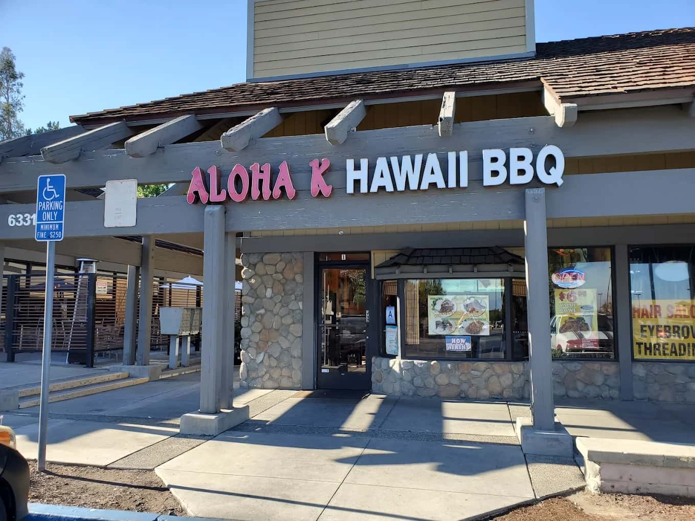 Storefront of Aloha K Hawaii BBQ with pink and white lettering above a stone-trimmed entrance
