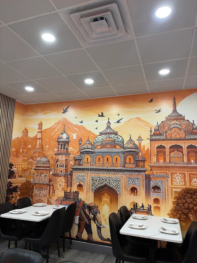 Dining room at AnTeRa Indian Kitchen with an orange mural of palaces and an elephant behind white tables