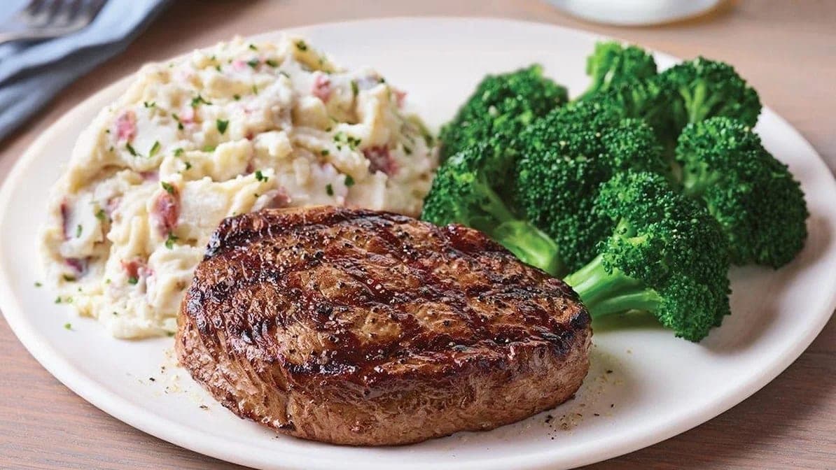 A grilled steak on a white plate with red-skin garlic mashed potatoes and steamed broccoli