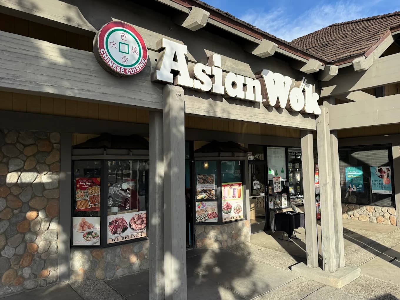 Storefront of Asian Wok with white block letters and a round Chinese Cuisine sign over a stone facade