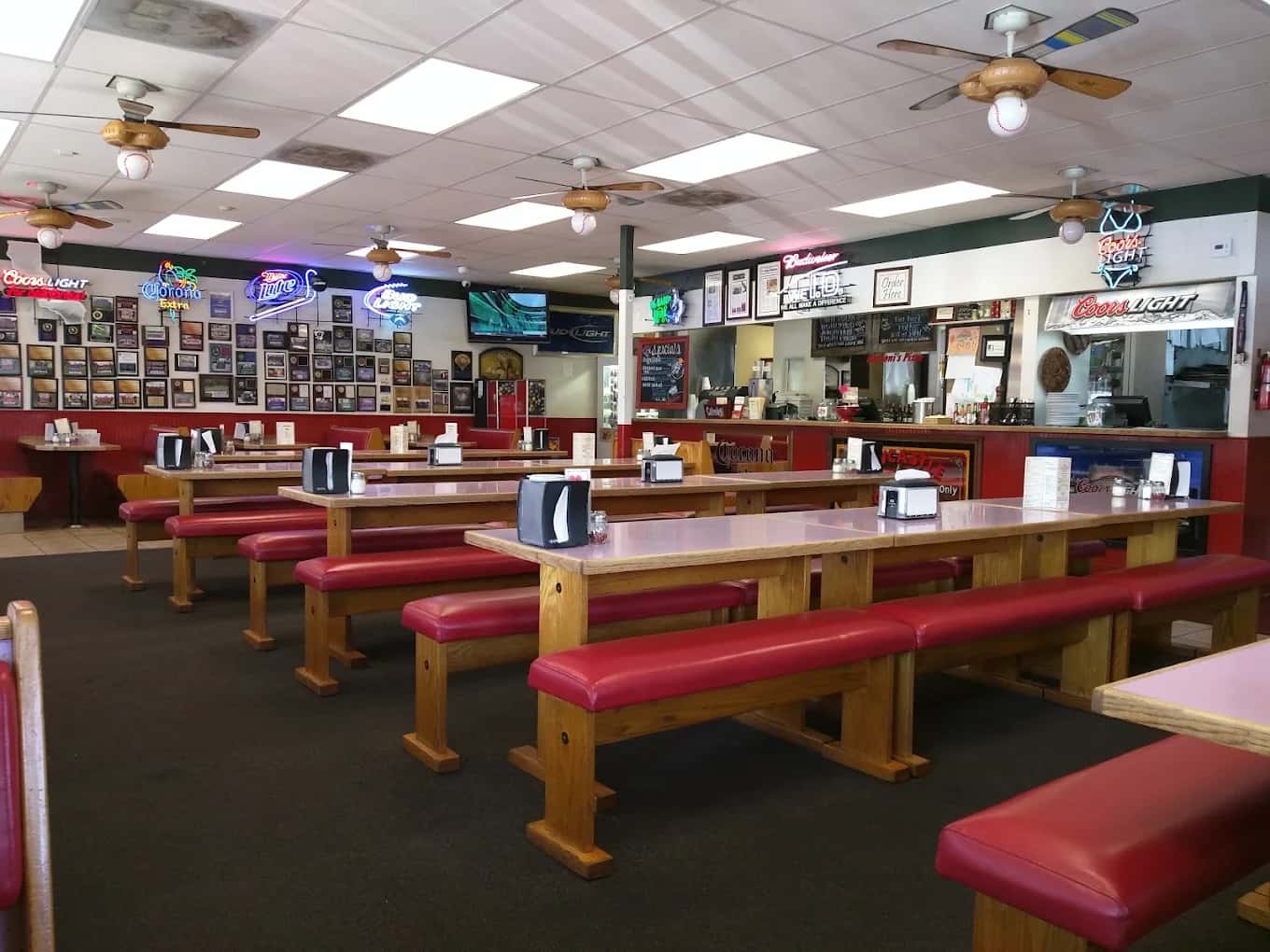 Dining room at Barboni's Pizza Alta Loma with long wooden tables, red benches and neon beer signs