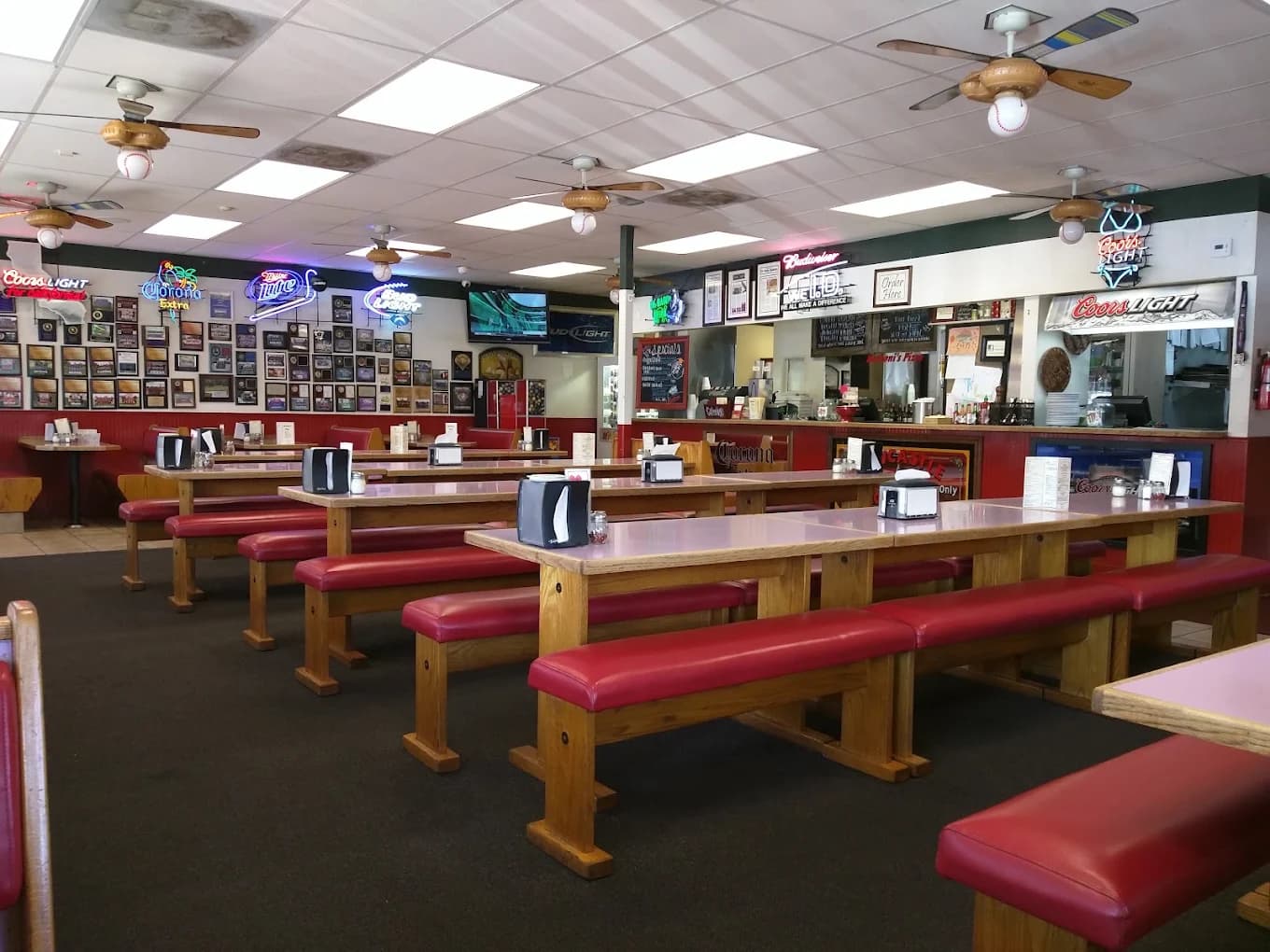 Dining room at Barboni's Pizza Alta Loma with long wooden tables, red benches and neon beer signs