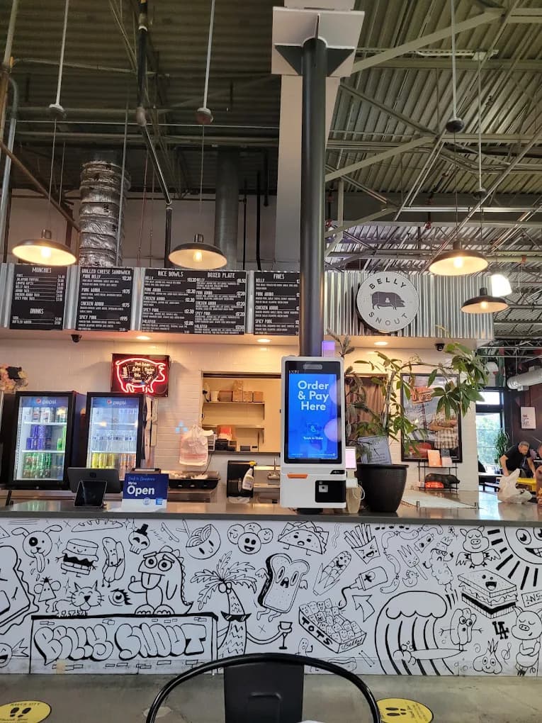 Order counter at Belly & Snout with a self-service kiosk, menu boards and a doodle-covered front