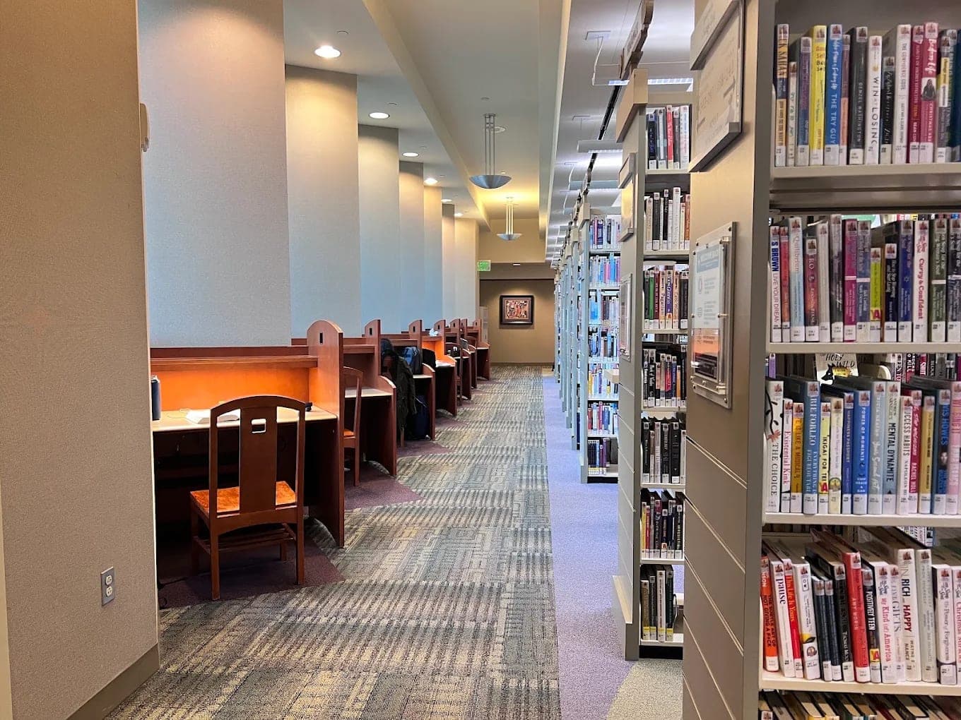 A reading aisle inside the Paul A. Biane Library, wooden study carrels along one wall and book stacks along the other