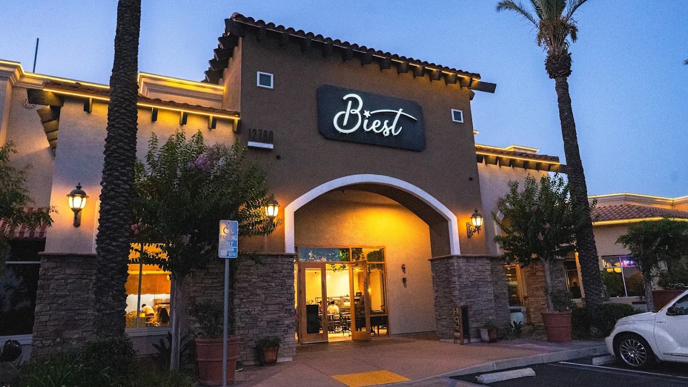Arched stucco entrance and lit sign of Biest Italian Kitchen at dusk, framed by palm trees