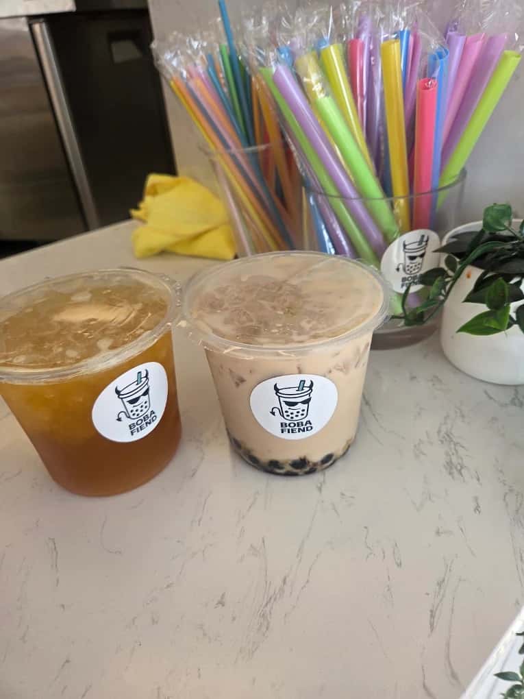Two sealed cups of iced tea and milk tea with boba beside a jar of colorful straws at Boba Fiend Tea House