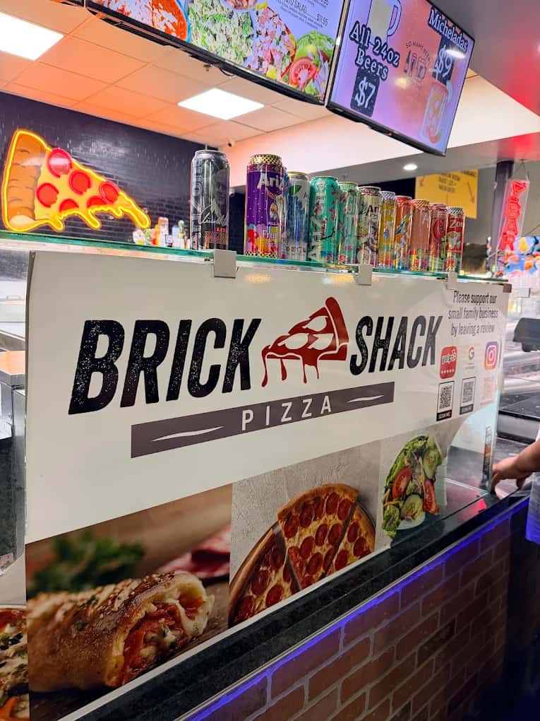 Front counter banner with pizza slice neon sign and canned drinks at Brick Shack Pizza
