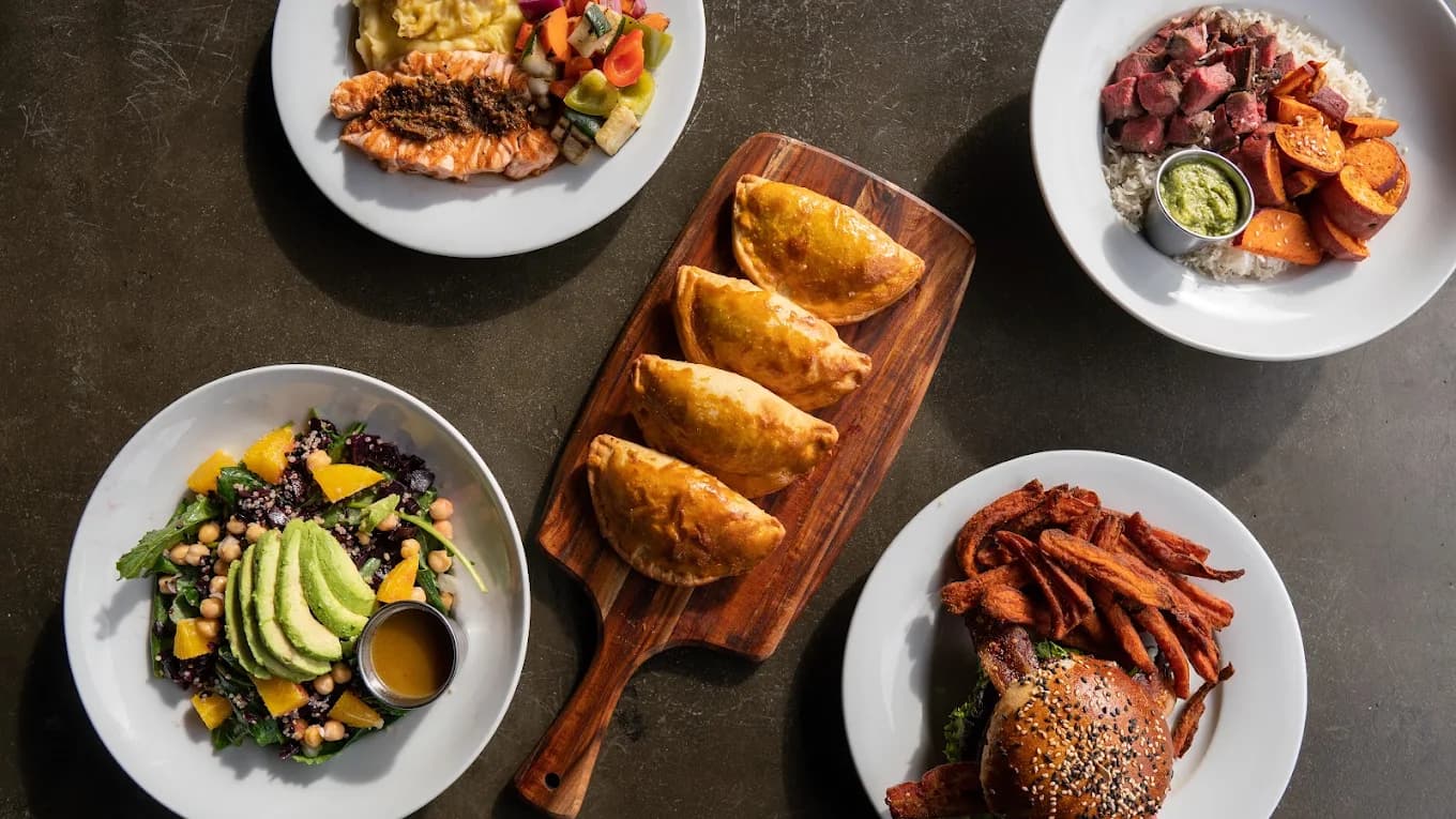Overhead spread of Bushfire Kitchen plates: salmon, salad with avocado, empanadas, a bowl and a burger with fries