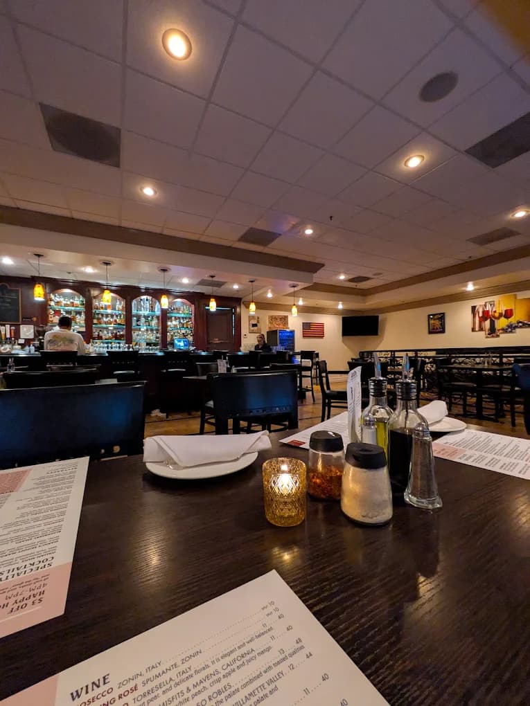 Dining room at Cara Mia with a wine menu on the table, oil and pepper shakers, and a bar in back