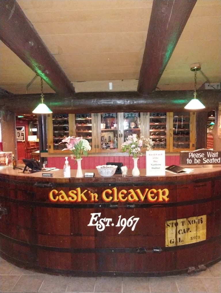 Barrel-style host stand lettered Cask 'n Cleaver Est. 1967 under exposed log beams