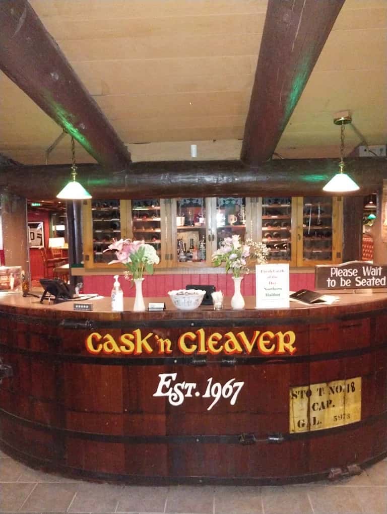 Barrel-style host stand lettered Cask 'n Cleaver Est. 1967 under exposed log beams