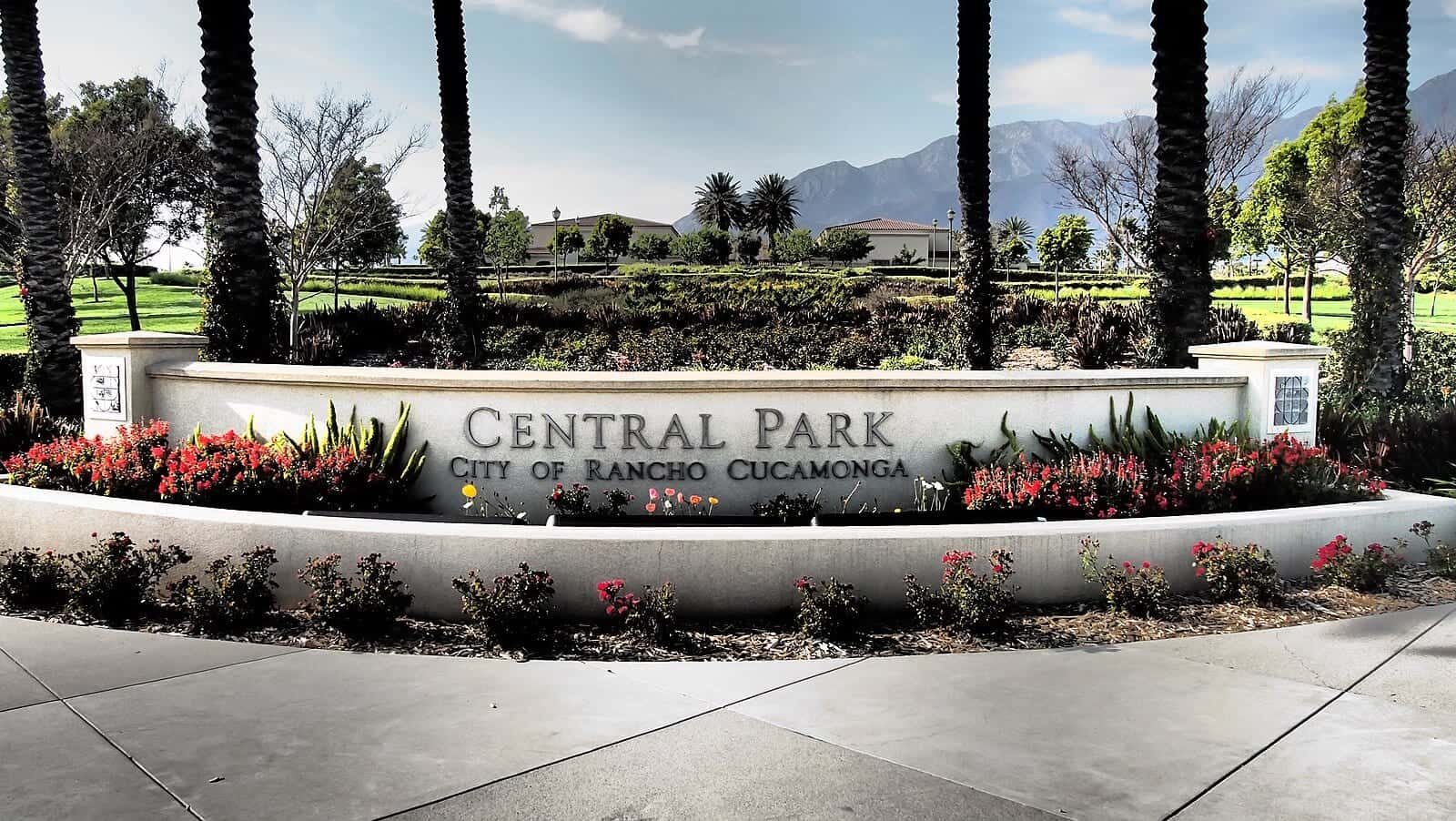 The curved stone entrance sign at Central Park, flowers and palms in front of open lawn with the mountains behind