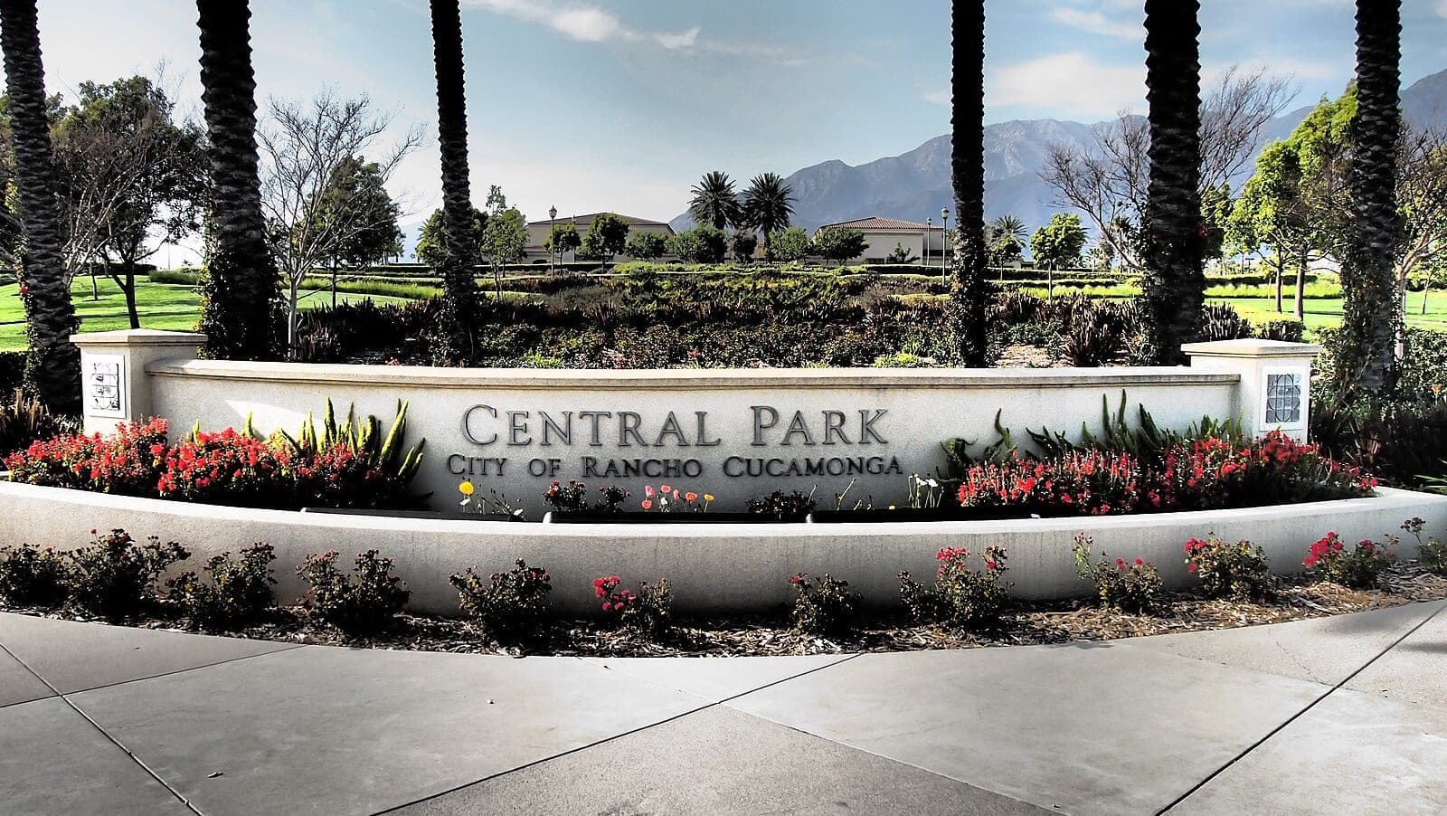 The curved stone entrance sign at Central Park, flowers and palms in front of open lawn with the mountains behind