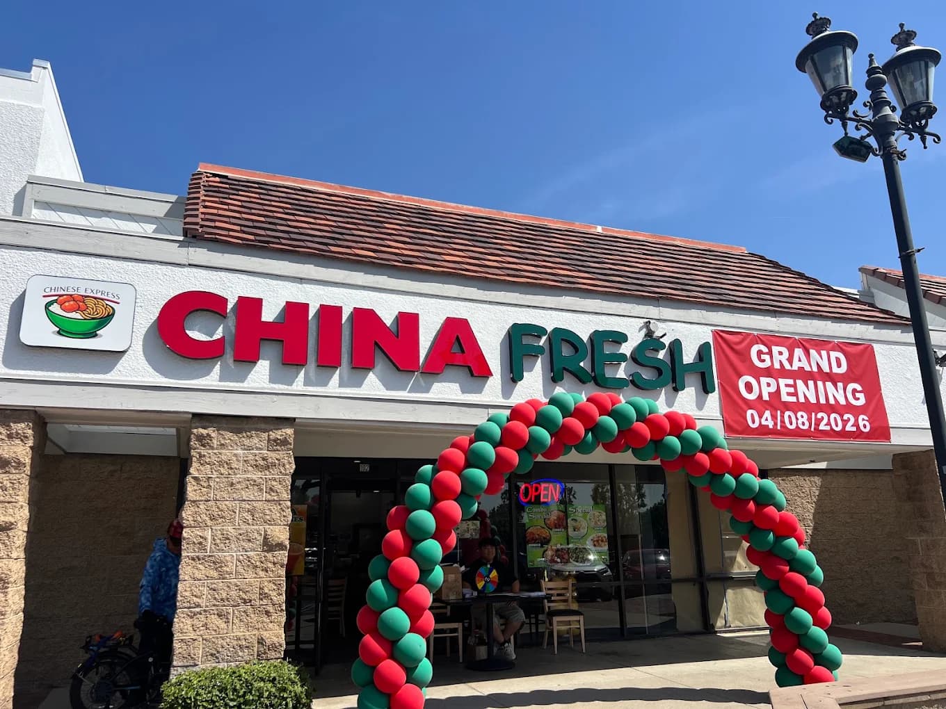 Storefront of China Fresh with a red and green balloon arch and a Grand Opening banner over the entrance