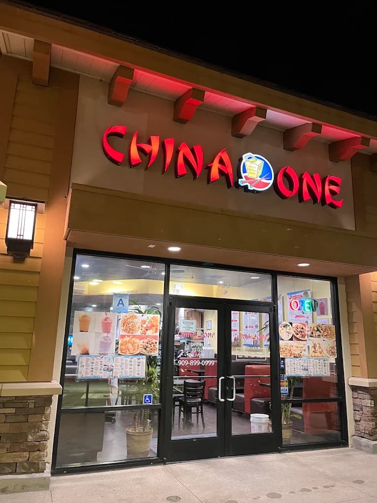 Lit red China One sign above glass entry doors covered with food posters at night