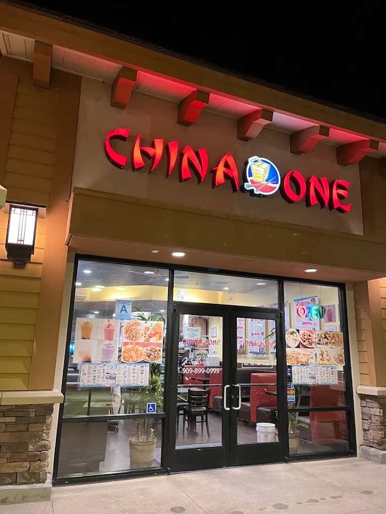 Lit red China One sign above glass entry doors covered with food posters at night
