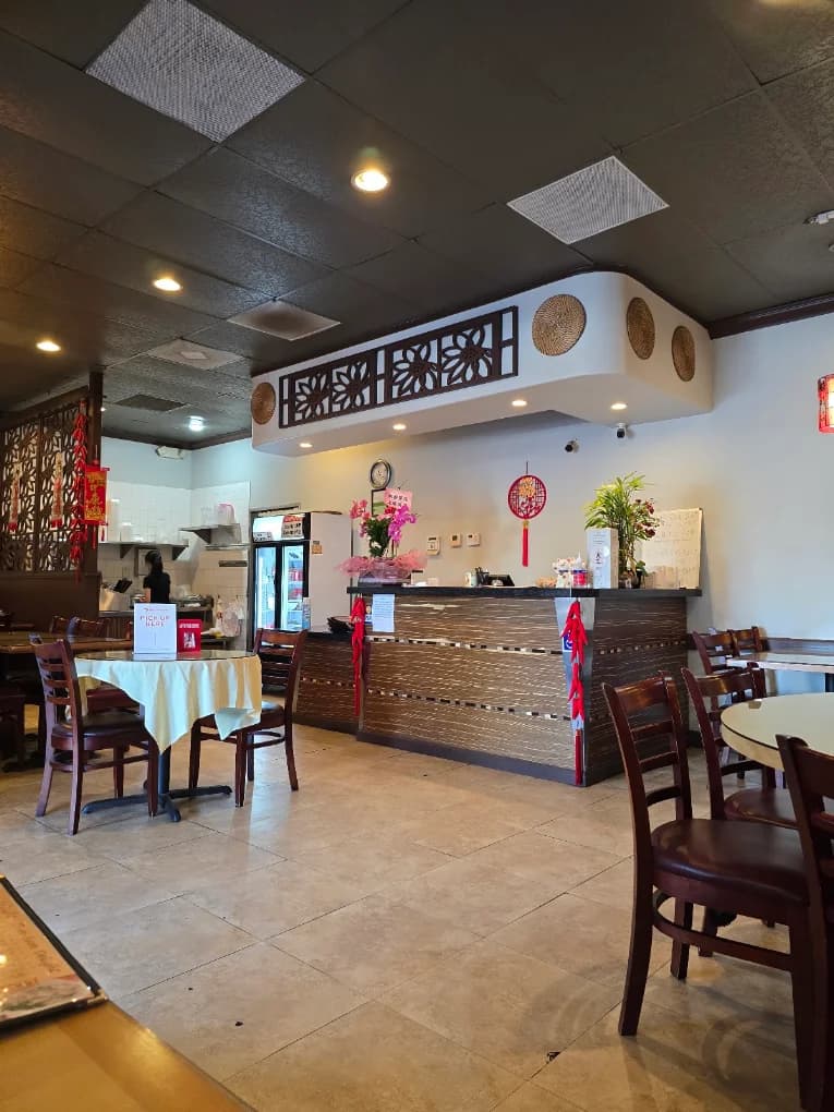 Dining room at China Pepper with a wood front counter, red lanterns, and tables with white tablecloths