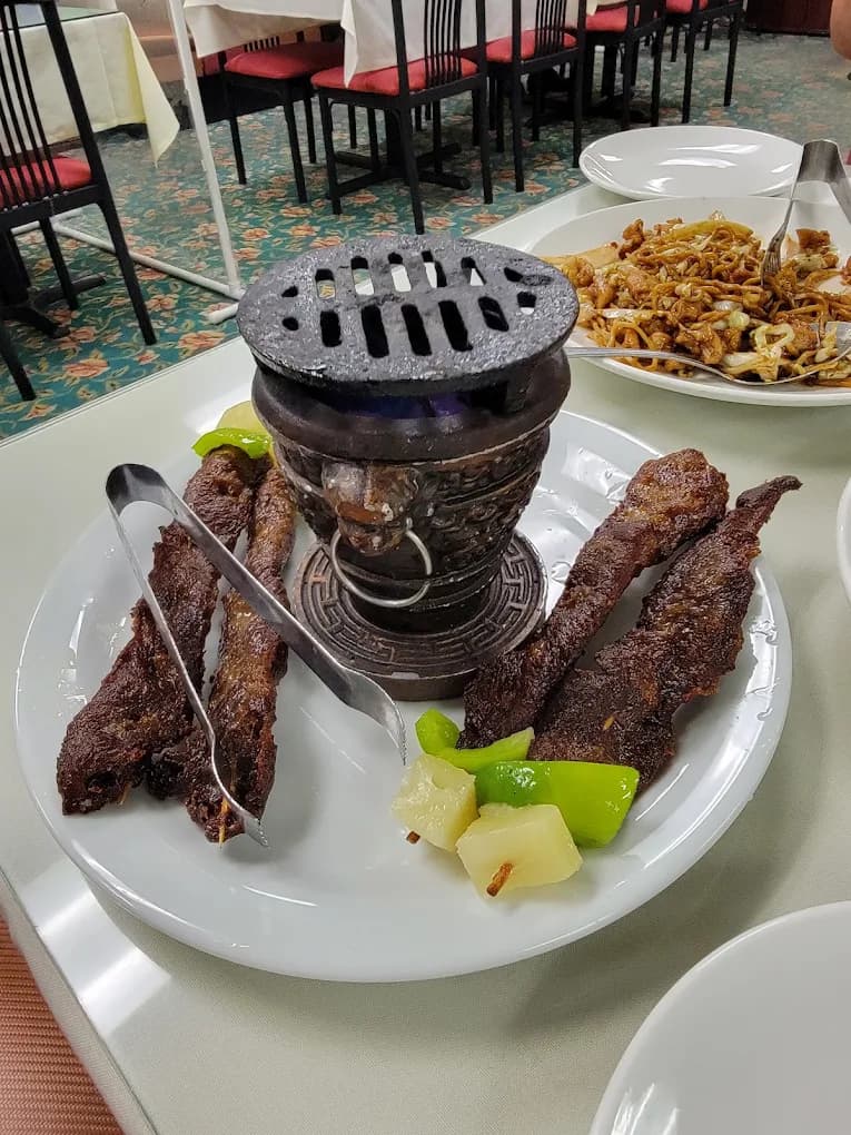 Grilled meat skewers around a small tabletop brazier with green peppers and pineapple at China Point
