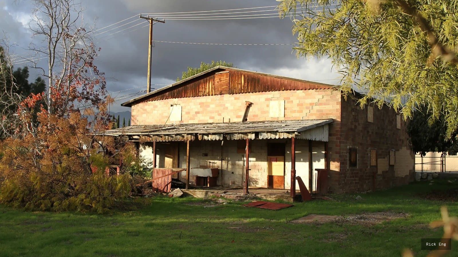 Weathered brick Chinatown House with boarded windows and a sagging corrugated porch roof under a stormy sky