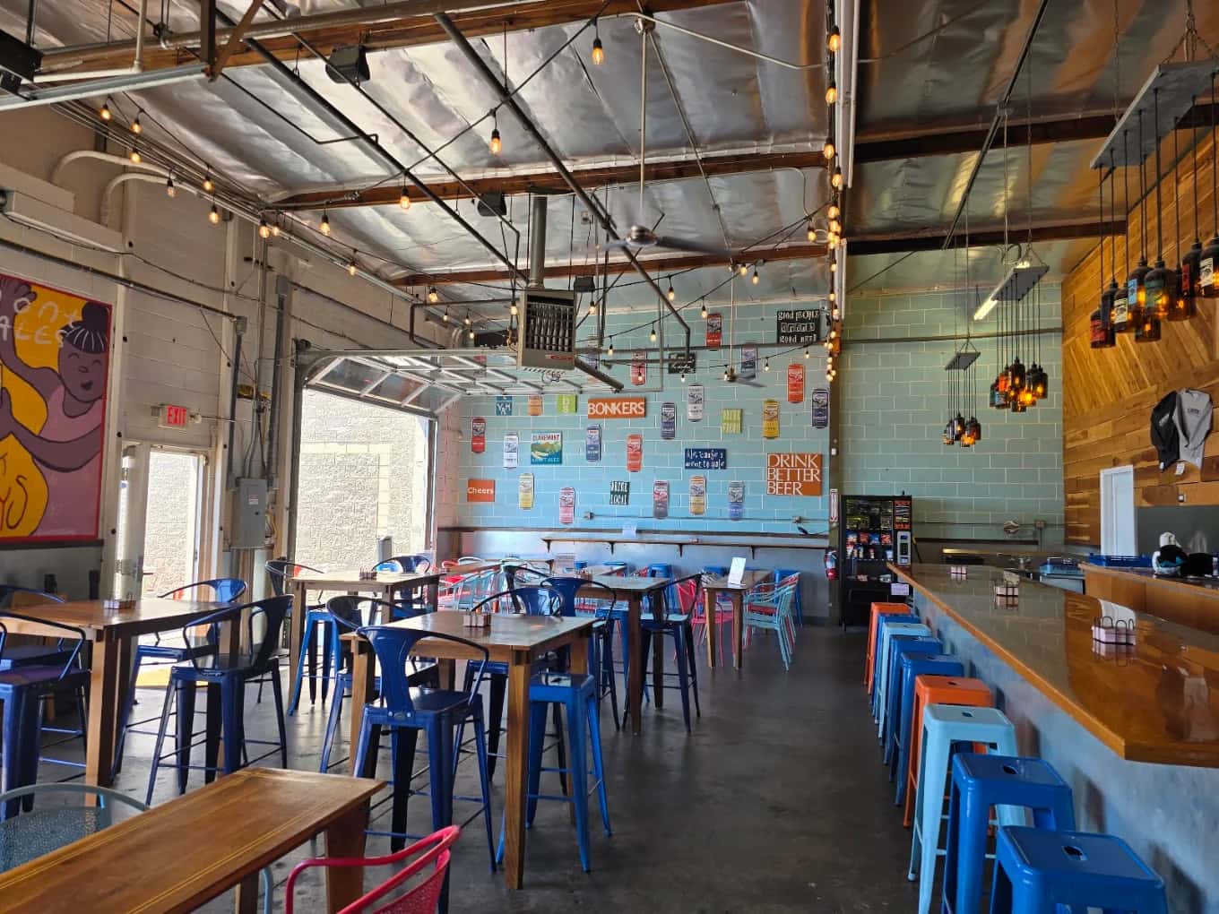 Claremont Craft Ales taproom with blue metal stools, wood tables, string lights and a can-covered wall