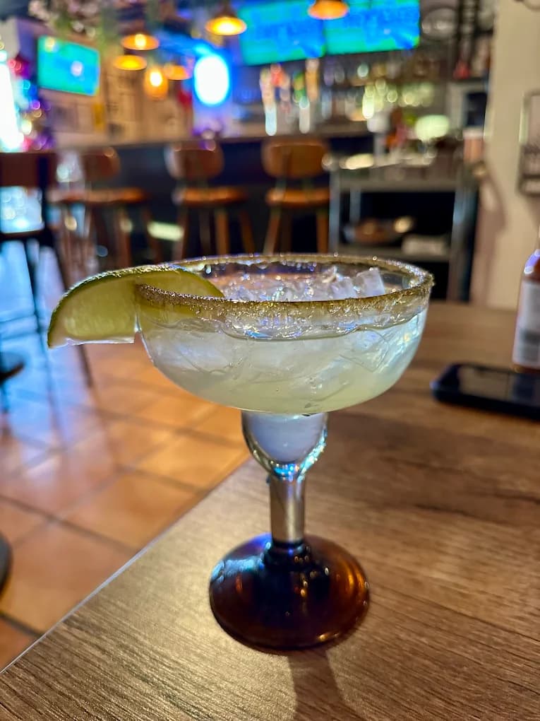 Margarita with a salted rim and lime wedge on a wood table at the bar of Cocina Serrano y Cantina
