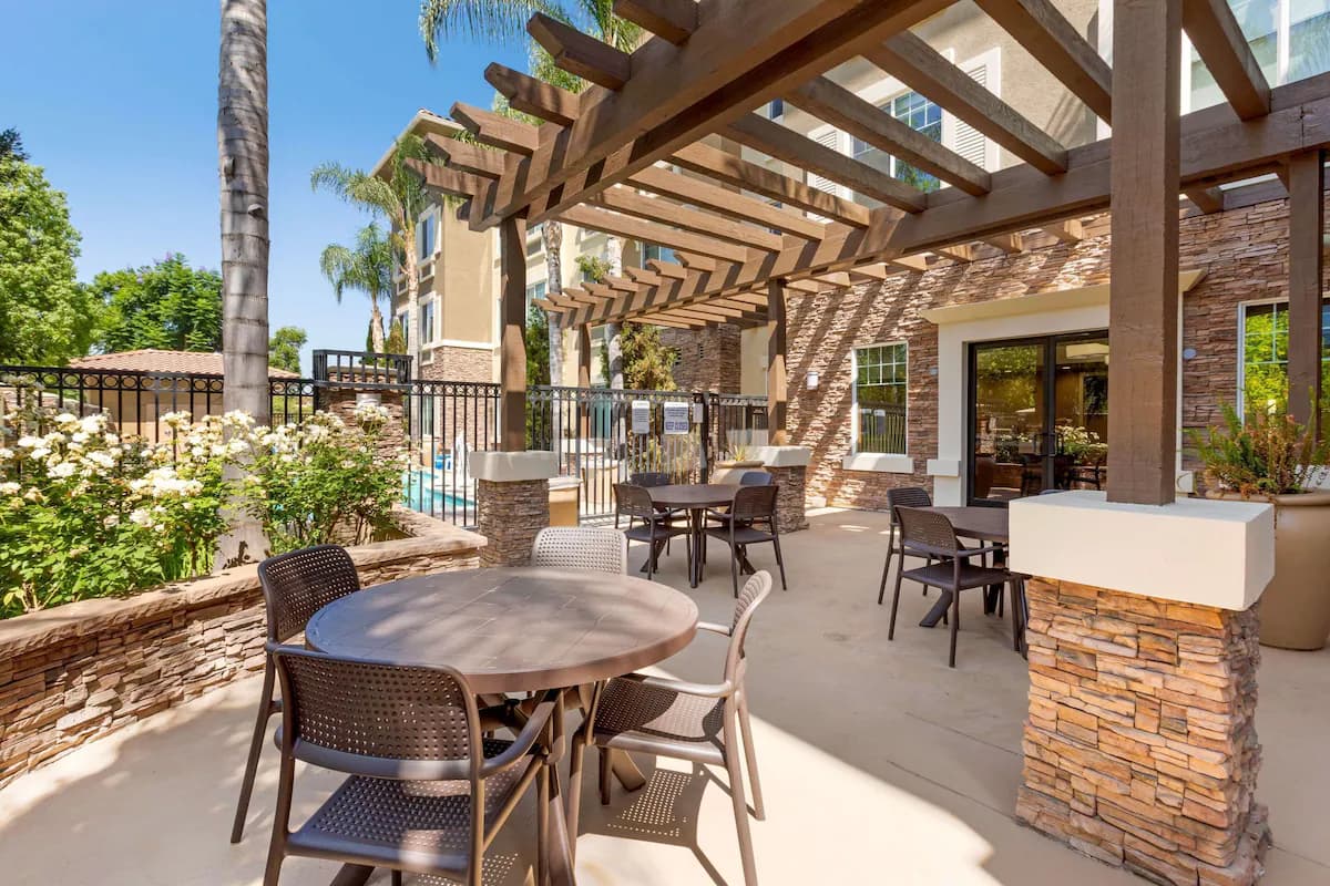 Outdoor patio with tables under a wood pergola beside the pool fence at Comfort Inn & Suites Near Ontario Airport