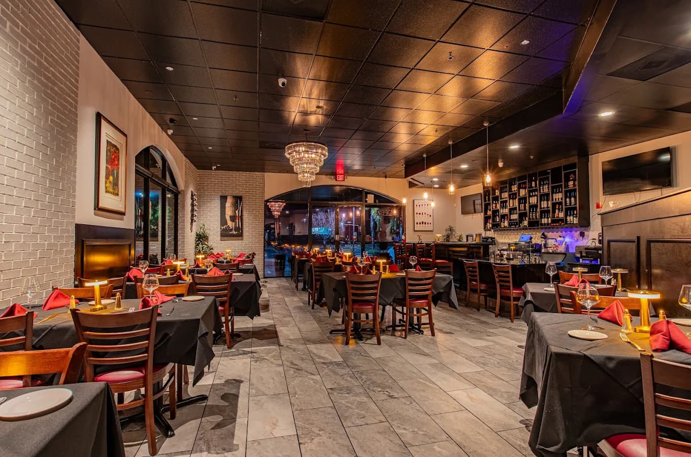 Dining room at Cornelio's Steak House with black tablecloths, red napkins, candle lamps and a wine wall behind the bar