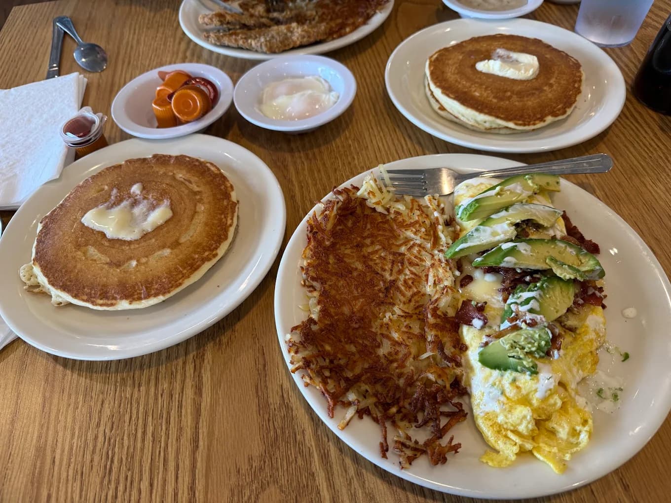 Buttermilk pancakes, hash browns and an avocado-topped omelet on a wood table at Country Kitchen Restaurant