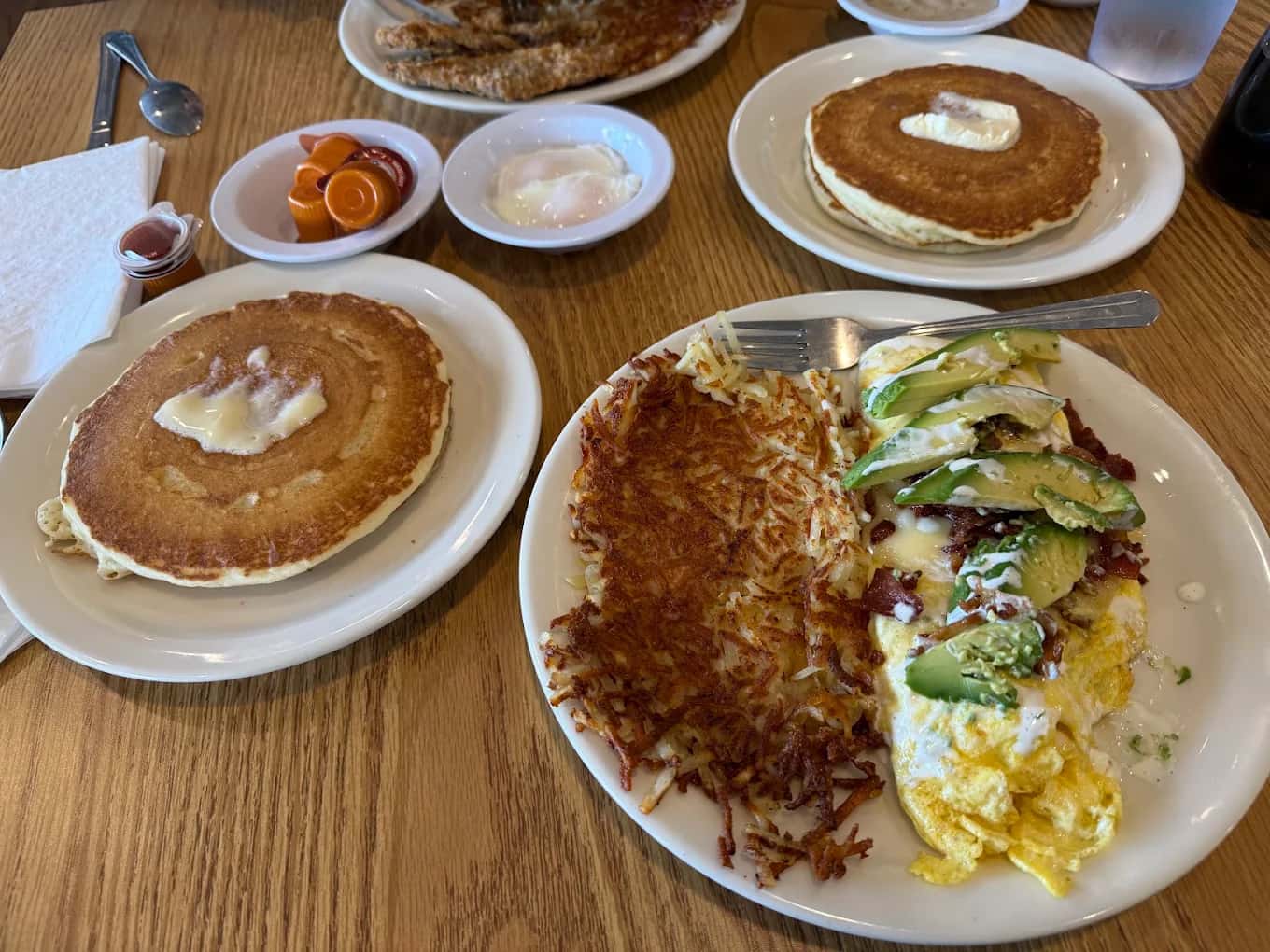 Buttermilk pancakes, hash browns and an avocado-topped omelet on a wood table at Country Kitchen Restaurant