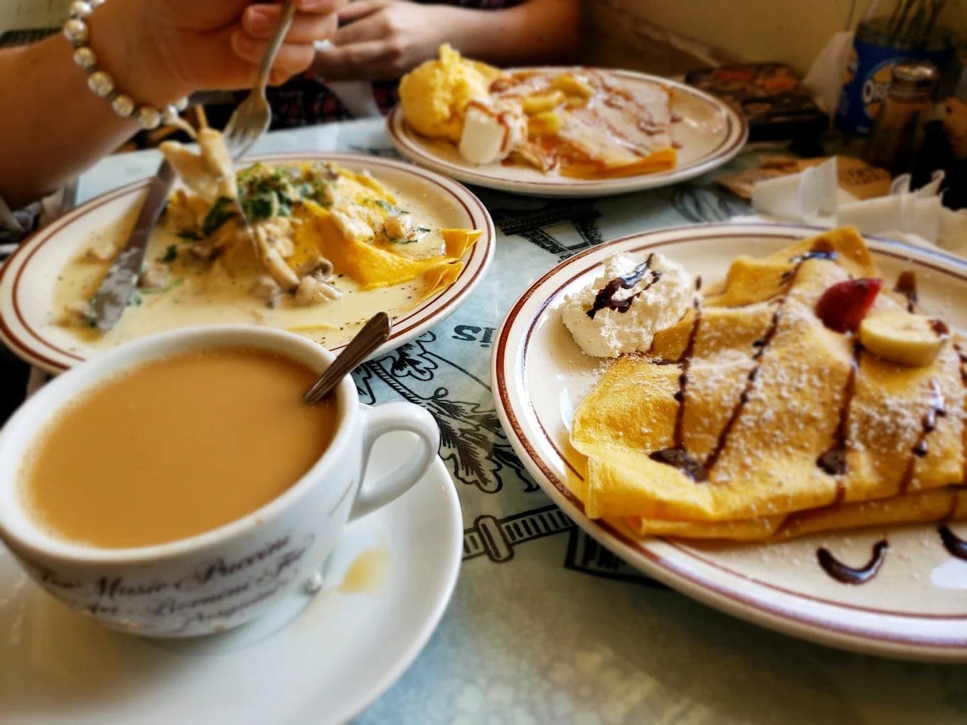 A table set with coffee, a savoury crepe in cream sauce and a sugar-dusted dessert crepe drizzled with chocolate