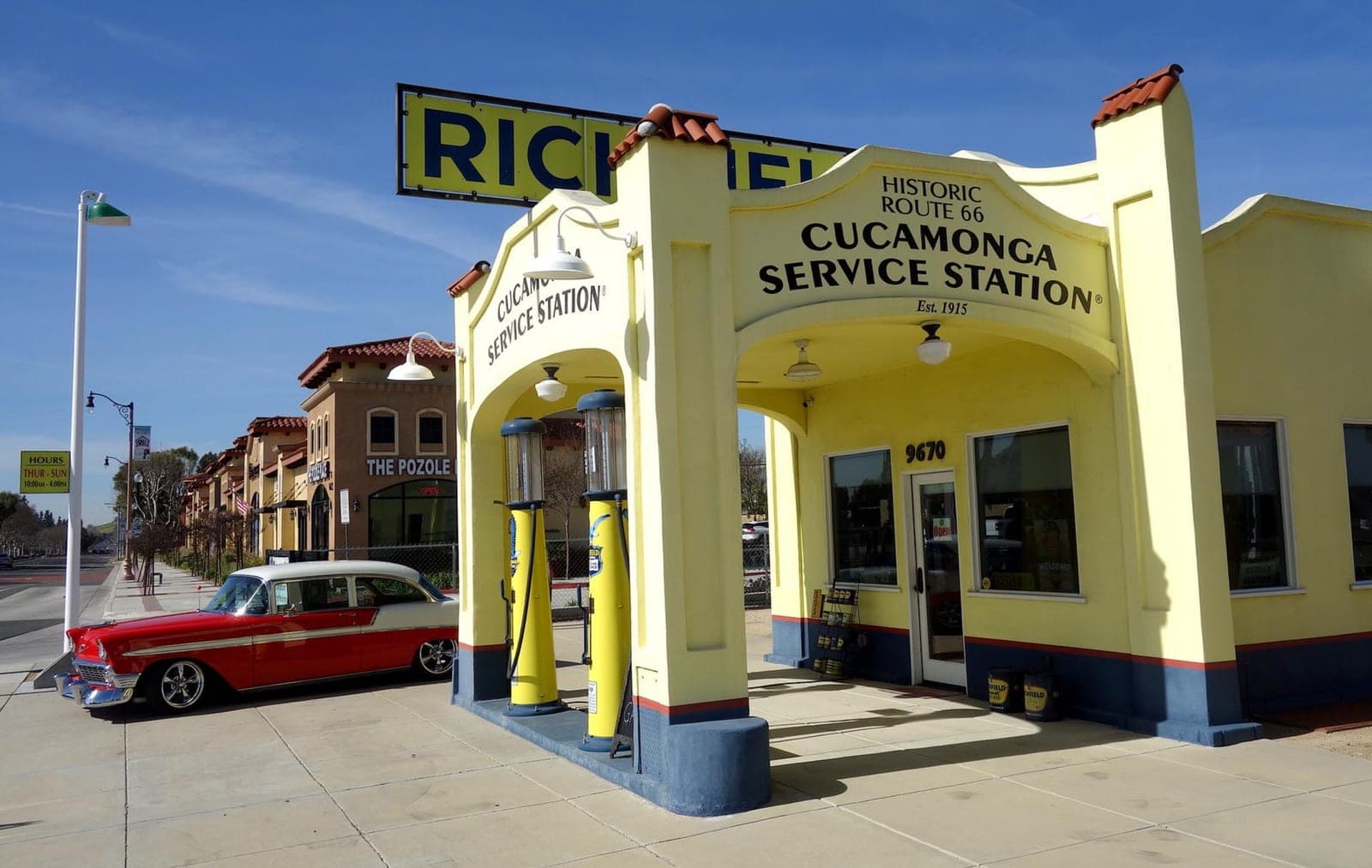 The restored Cucamonga Service Station on Route 66, its yellow Richfield canopy and 1915 arches beside a red and white 1956 Chevrolet