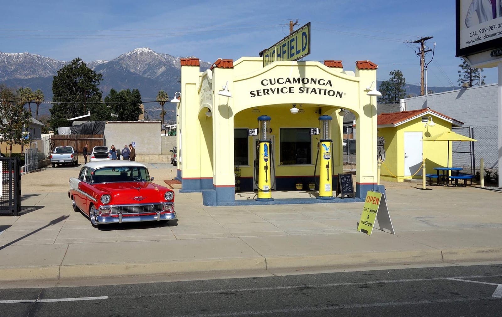 The Cucamonga Service Station seen from Foothill Boulevard with snow on Cucamonga Peak behind it and a red 1956 Chevrolet parked out front