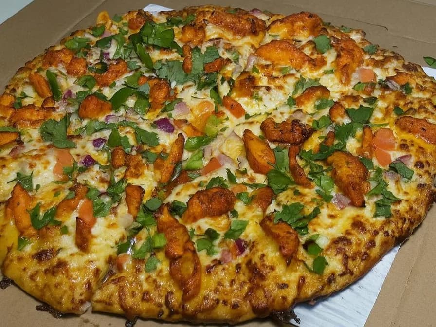Pizza topped with spiced chicken, red onion, tomato and cilantro in a box from Desi Pizza Bite