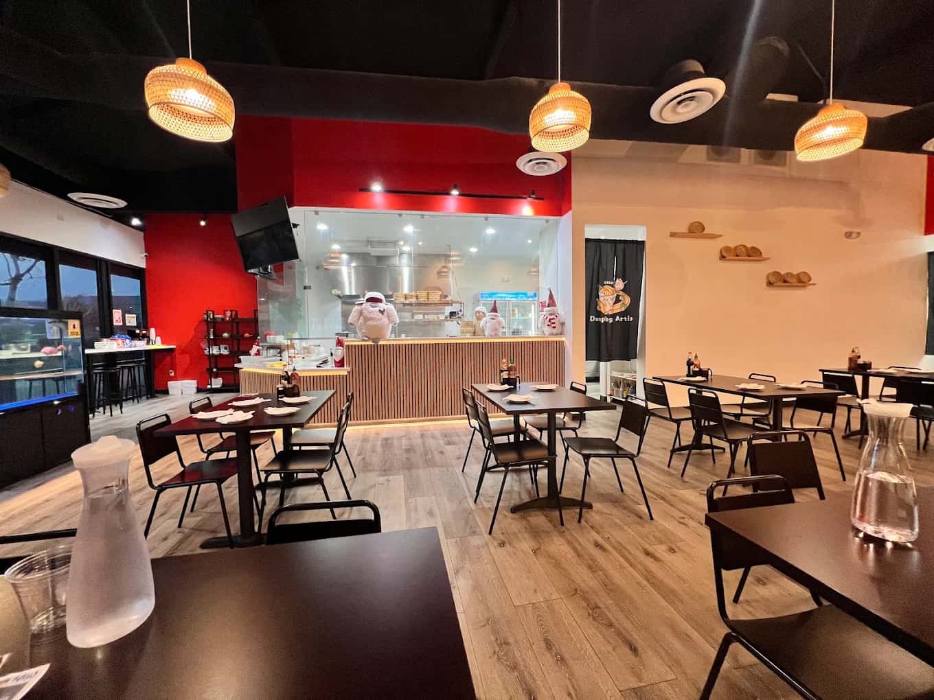 Dining room at Dumpling Artisan with black tables, woven pendant lights and a red wall by the kitchen window