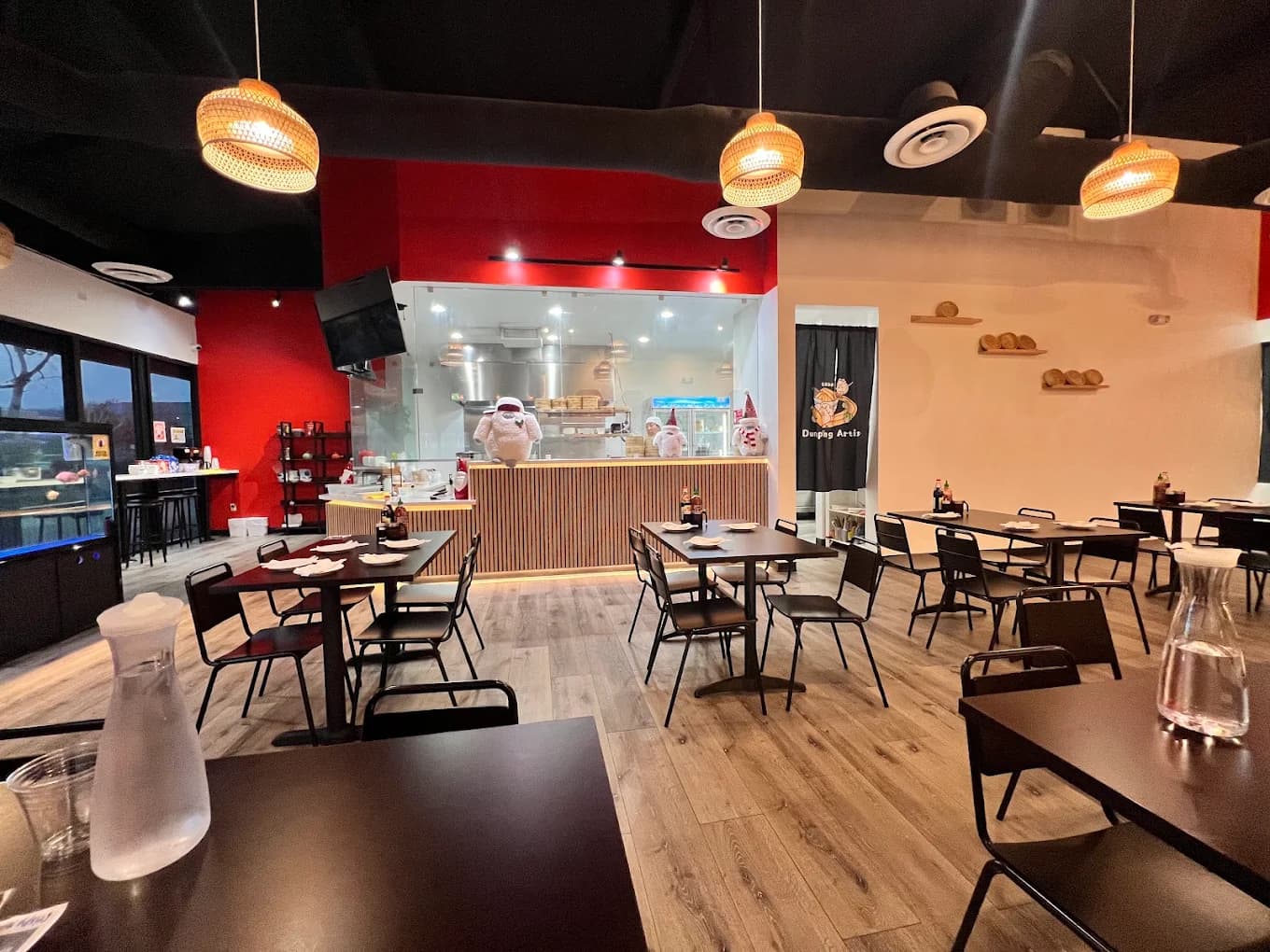 Dining room at Dumpling Artisan with black tables, woven pendant lights and a red wall by the kitchen window
