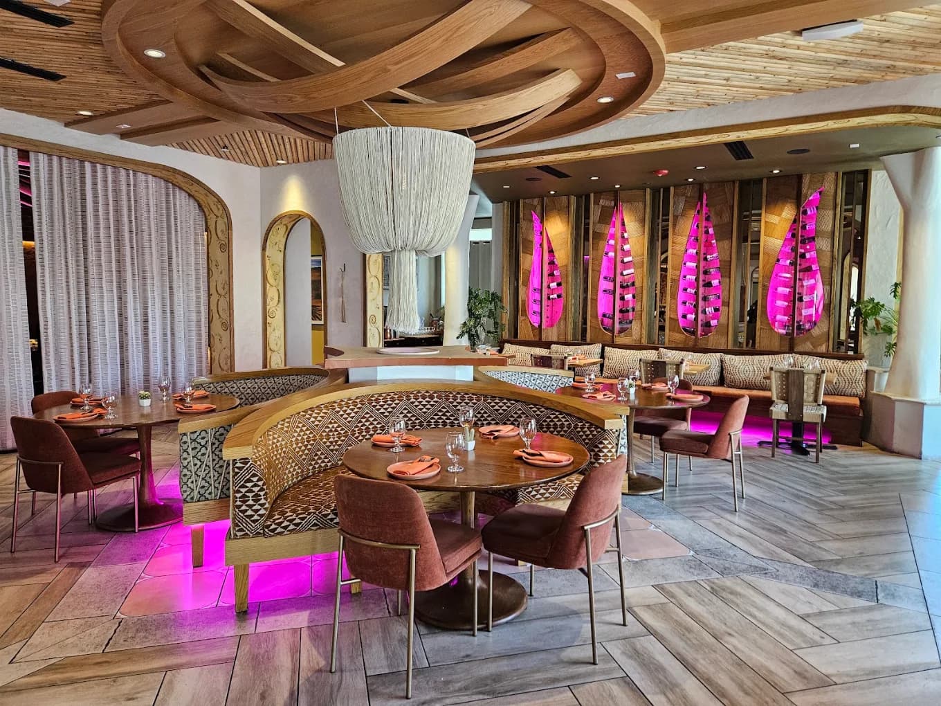 Dining room at Durango Cocina & Rooftop with curved booths, round tables and pink-lit wine displays