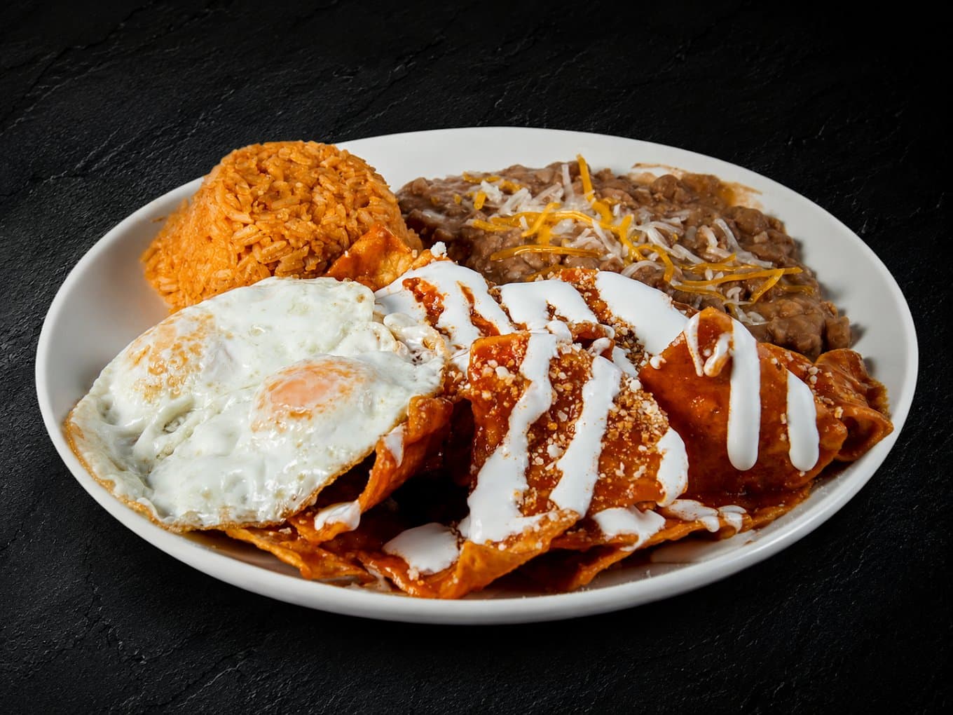 Chilaquiles with fried eggs, rice and refried beans on a white plate from Fuego Cravings