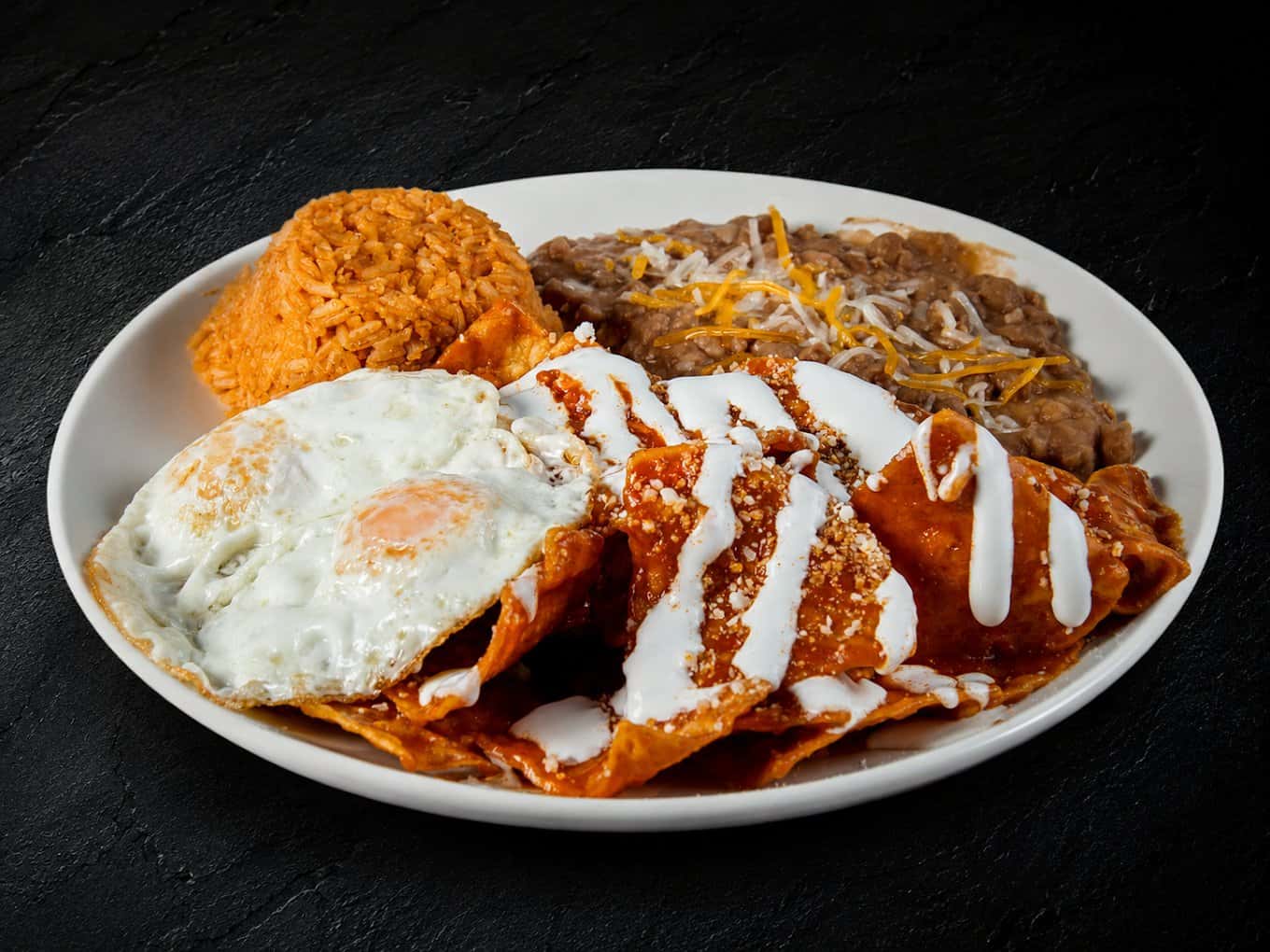 Chilaquiles with fried eggs, rice and refried beans on a white plate from Fuego Cravings
