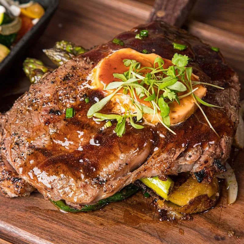 Grilled steak topped with butter and herbs over asparagus on a wooden board at Gina's Kitchen