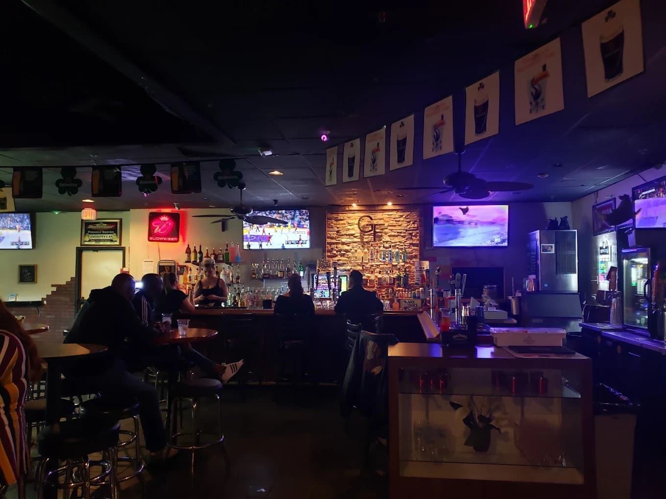 Dim bar interior with patrons on stools, TVs and shamrock banners at Good Fella's
