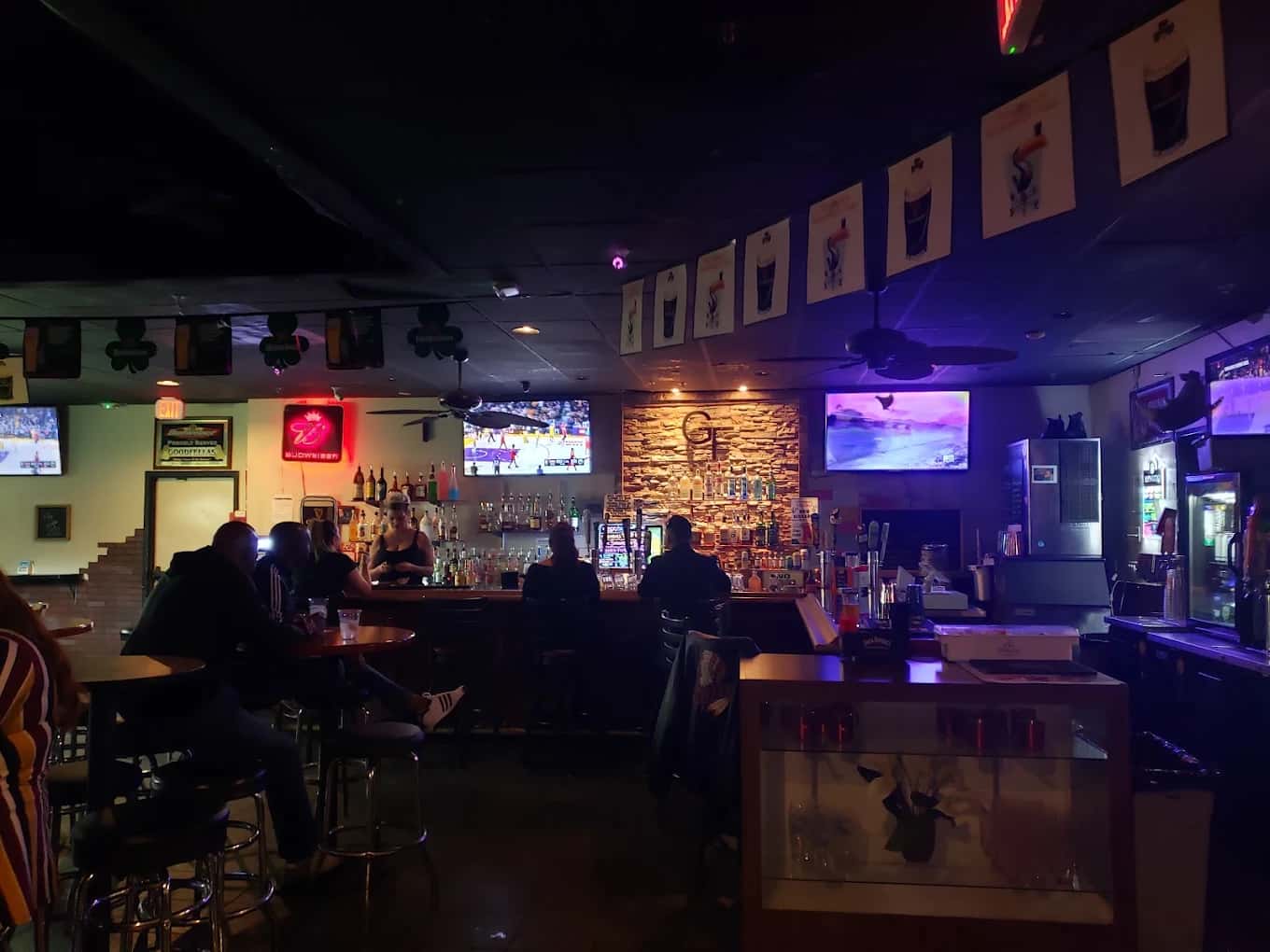 Dim bar interior with patrons on stools, TVs and shamrock banners at Good Fella's