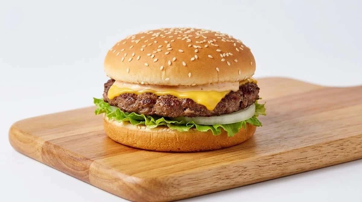 A cheeseburger on a wooden board, sesame bun over a beef patty with melted cheese, lettuce and onion