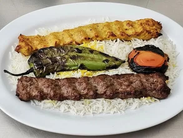 Plate of two kabobs with a grilled pepper and tomato over saffron rice at Habibi Kabob