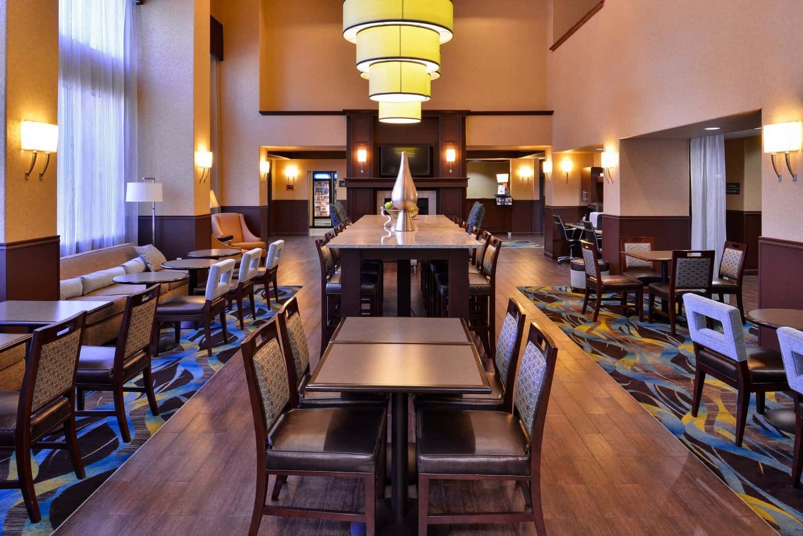 Dining area at the Hampton Inn & Suites Ontario with small tables, a tall communal table and yellow pendant lights