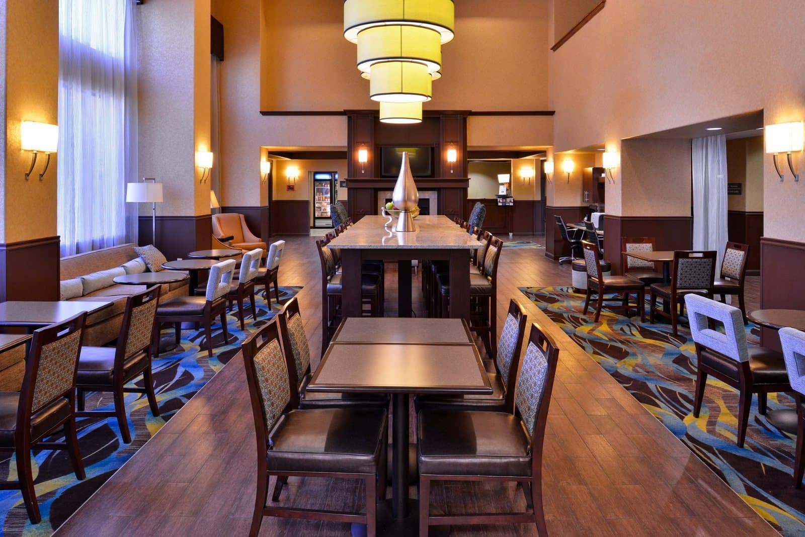 Dining area at the Hampton Inn & Suites Ontario with small tables, a tall communal table and yellow pendant lights