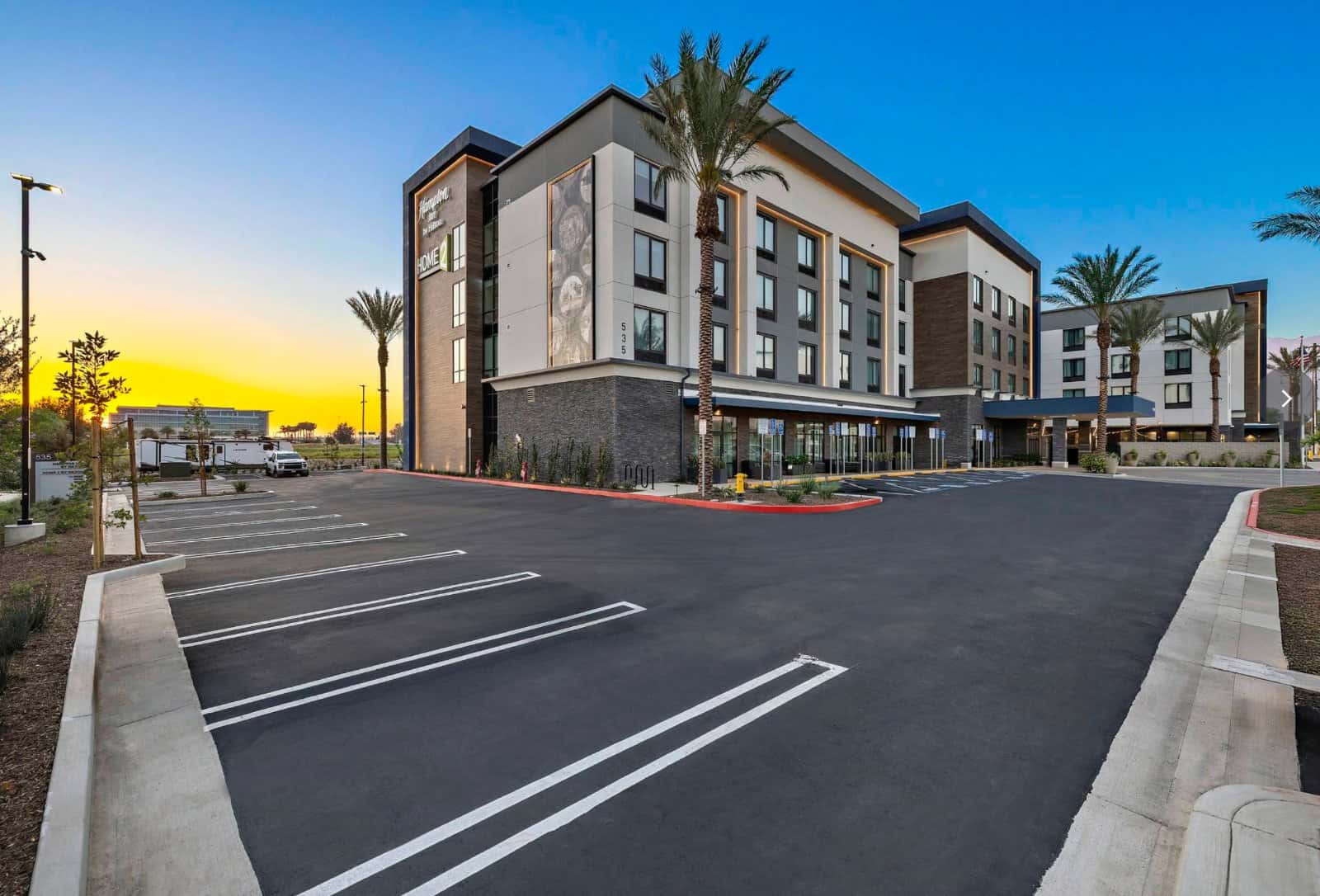 Exterior and parking lot of Hampton Inn by Hilton Ontario Airport with palm trees at dusk