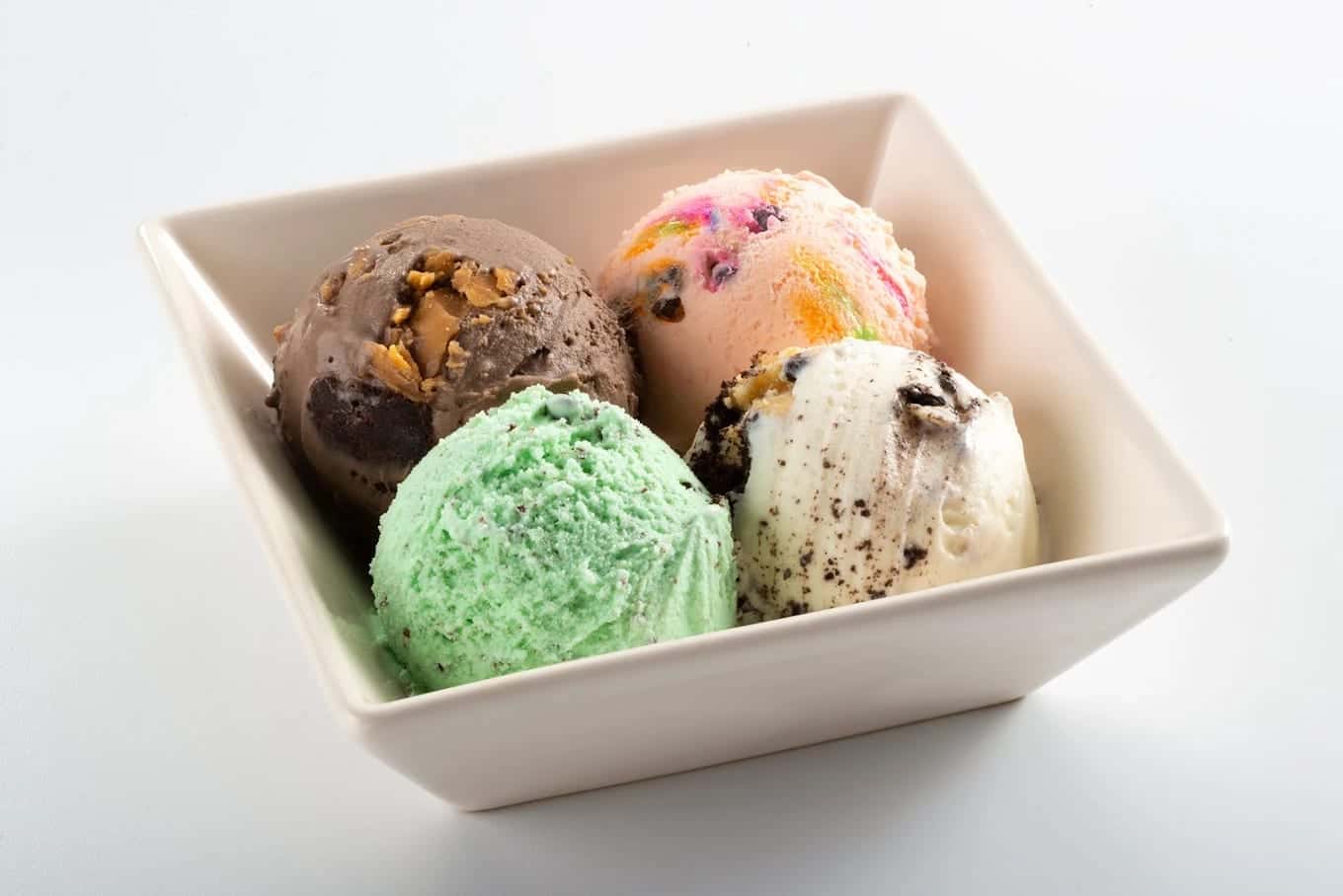 Four scoops in a square white bowl: chocolate with nuts, a rainbow flavour, mint and cookies and cream